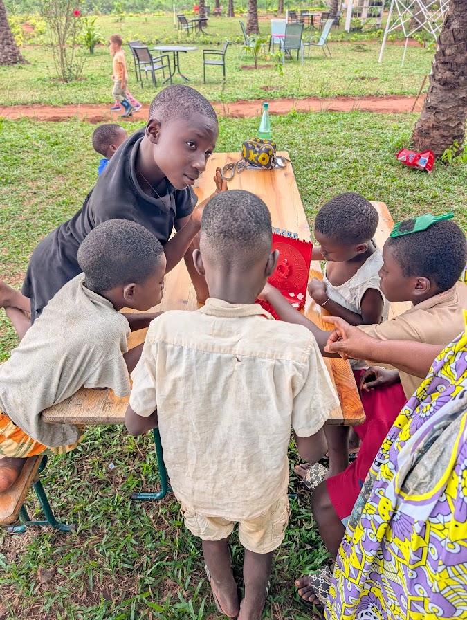 Des enfants du village réunis autour d'un jeu, accompagnés d'une animatrice